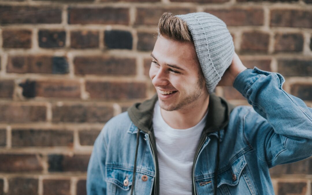 man holding the back of his head while smiling near brick wall
