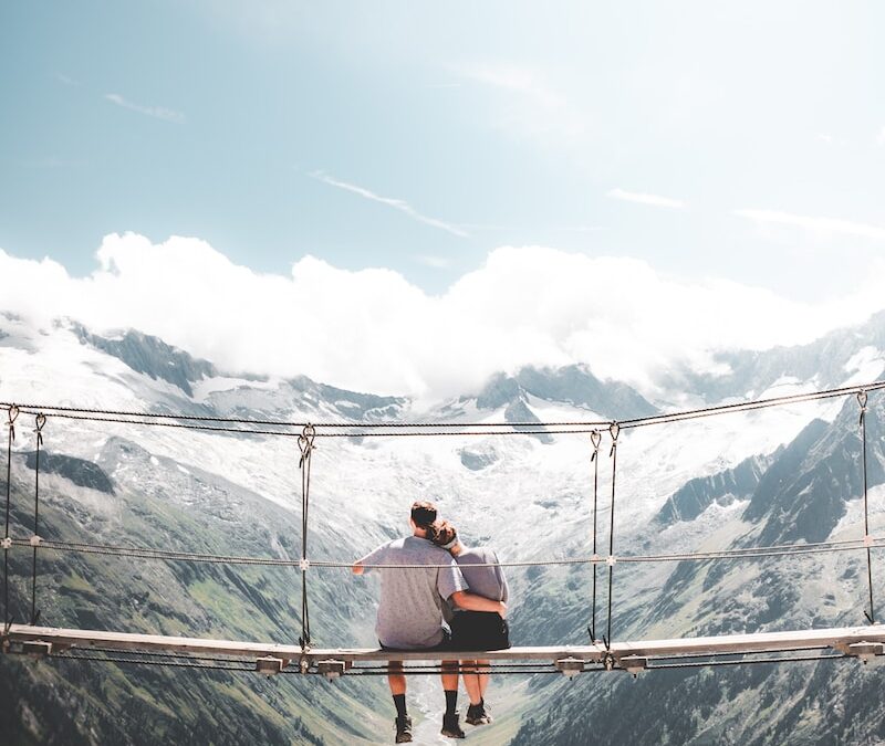 man and woman sitting on hanging bridge at daytime